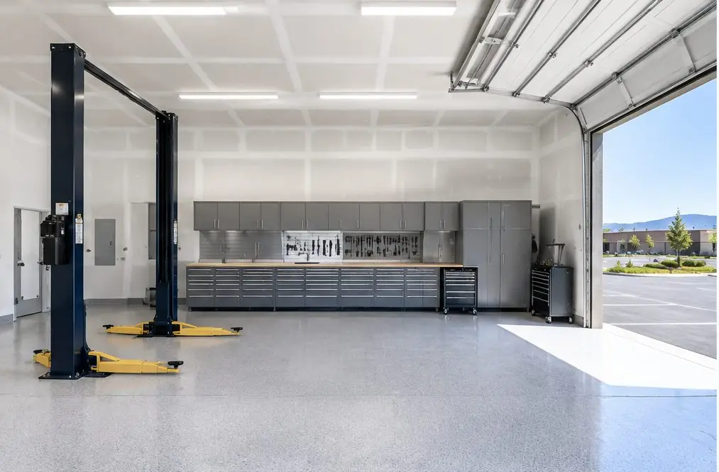 Illustration: an auto repair bay in Menifee, CA with a wall of gray steel drawer cabinets, a steel-topped bench, a two-post lift at one side and a roll-up door open on a parking lot